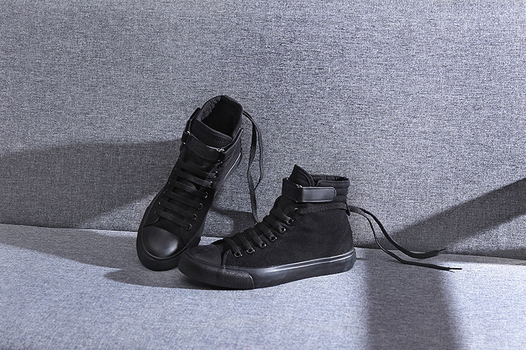 Pair of black high-top sneakers on a gray surface with a neutral background