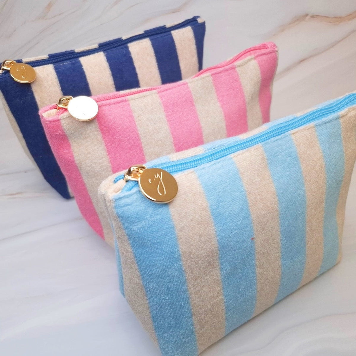 Three striped pouches in blue, pink, and blue and beige on a light wooden surface.