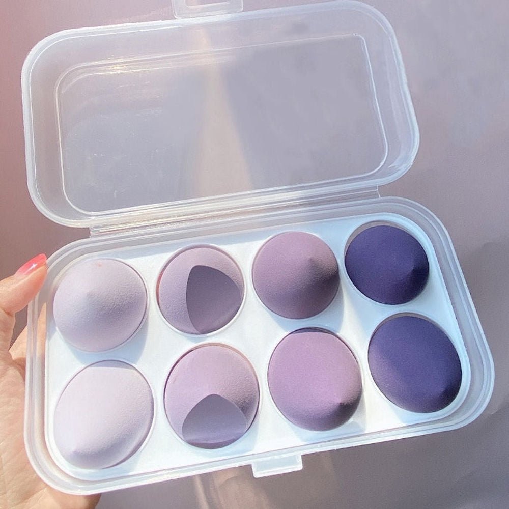 Set of purple makeup sponges in a clear plastic case held by a hand.