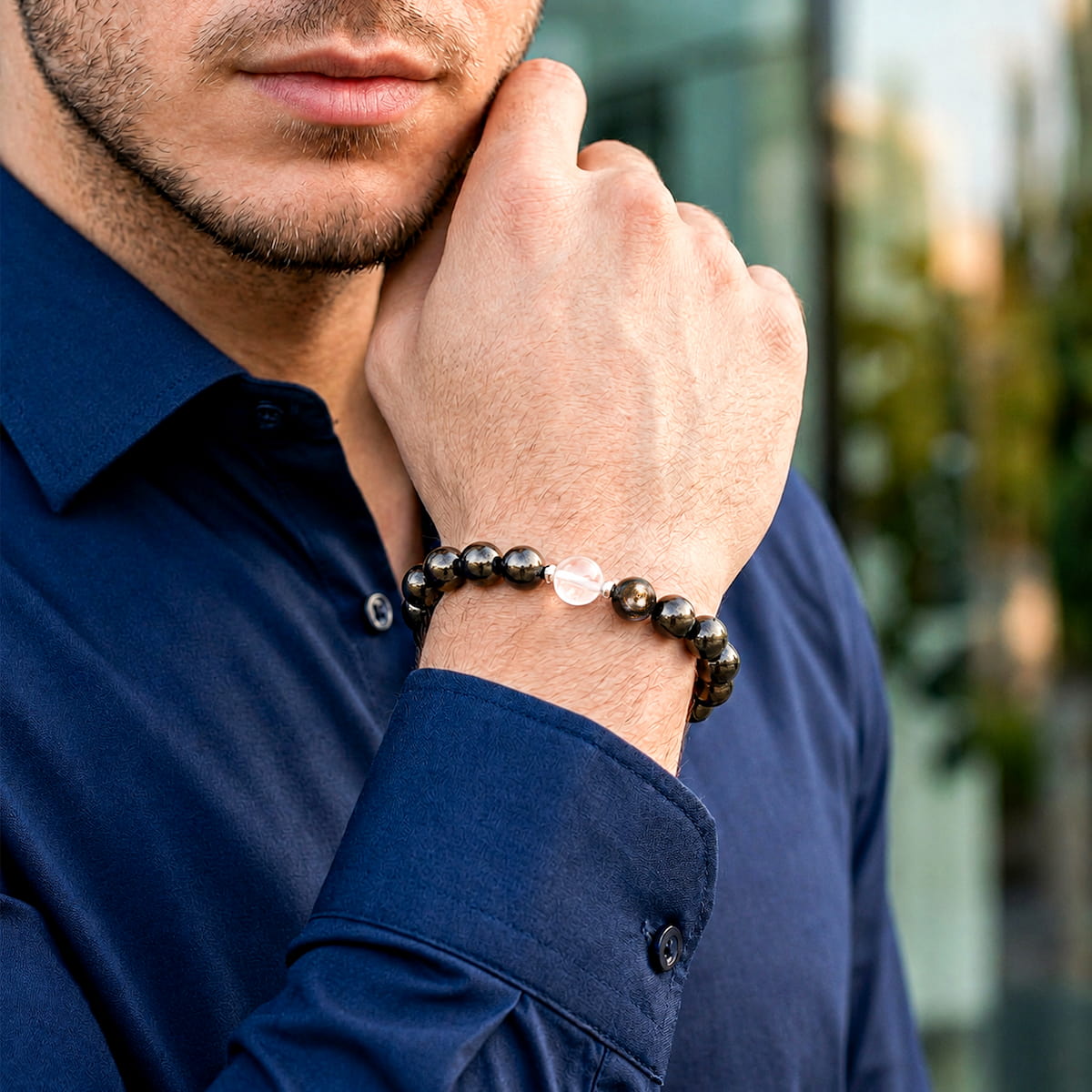 A man wearing a dark beaded bracelet with a clear teardrop-shaped crystal pendant, paired with a navy blue button-down shirt. The Hypersthene Millionaire Manifestation Bracelet - Rare Egyptian Wealth Stone
