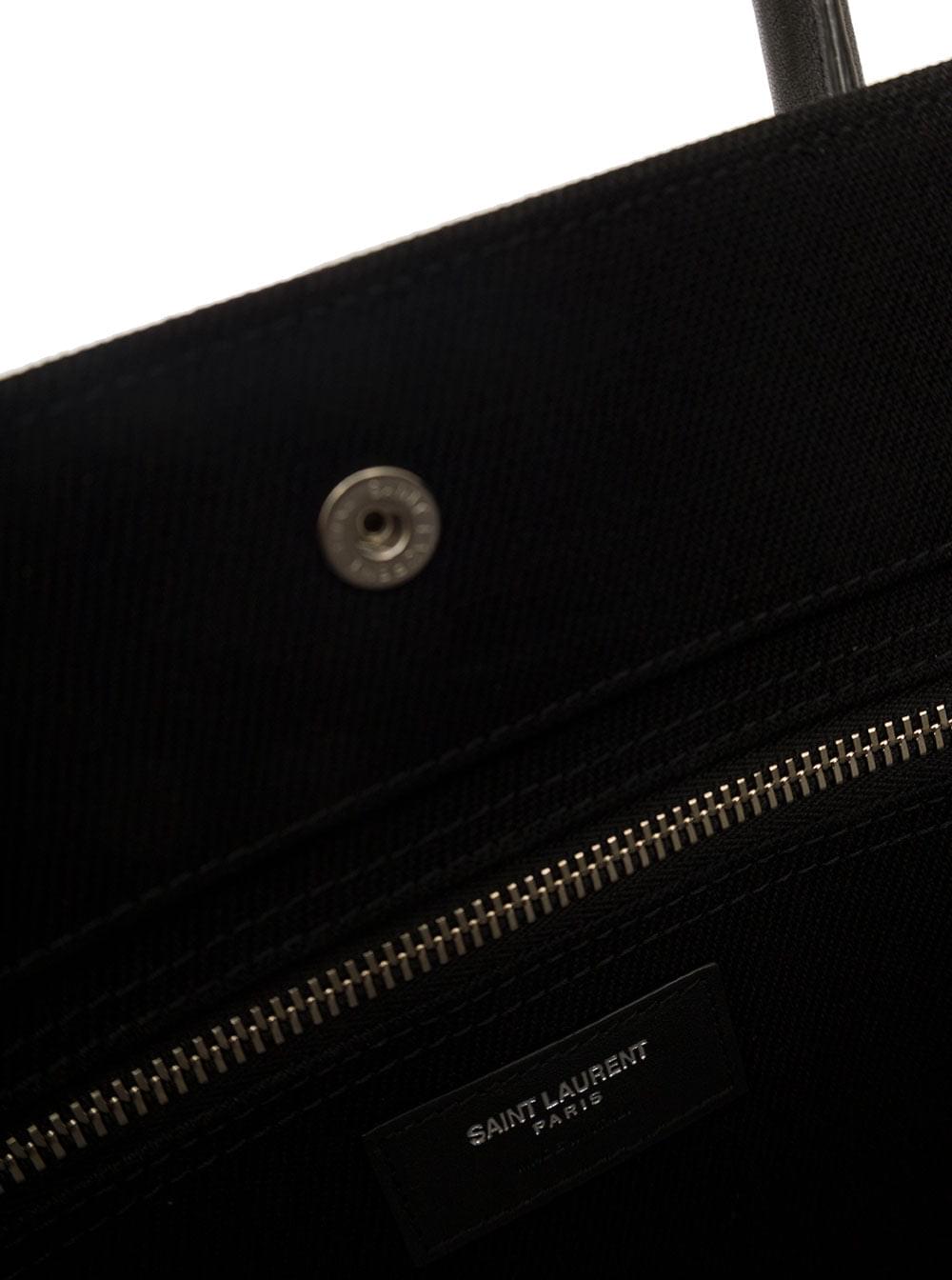 Close-up view of the Saint Laurent 'Rive Gauche' tote bag featuring a silver-tone metal snap closure, a silver zipper, and the signature white Saint Laurent brand label, shot against a clean white background.