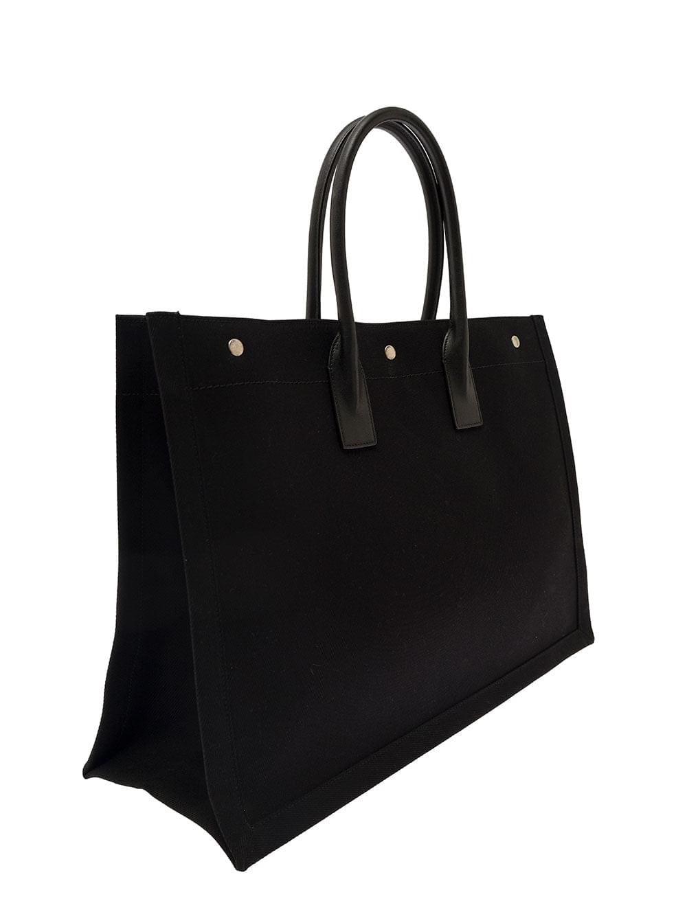 Saint Laurent Rive Gauche black cotton tote bag featuring two leather top handles and a contrasting white logo print, displayed against a clean white background.
