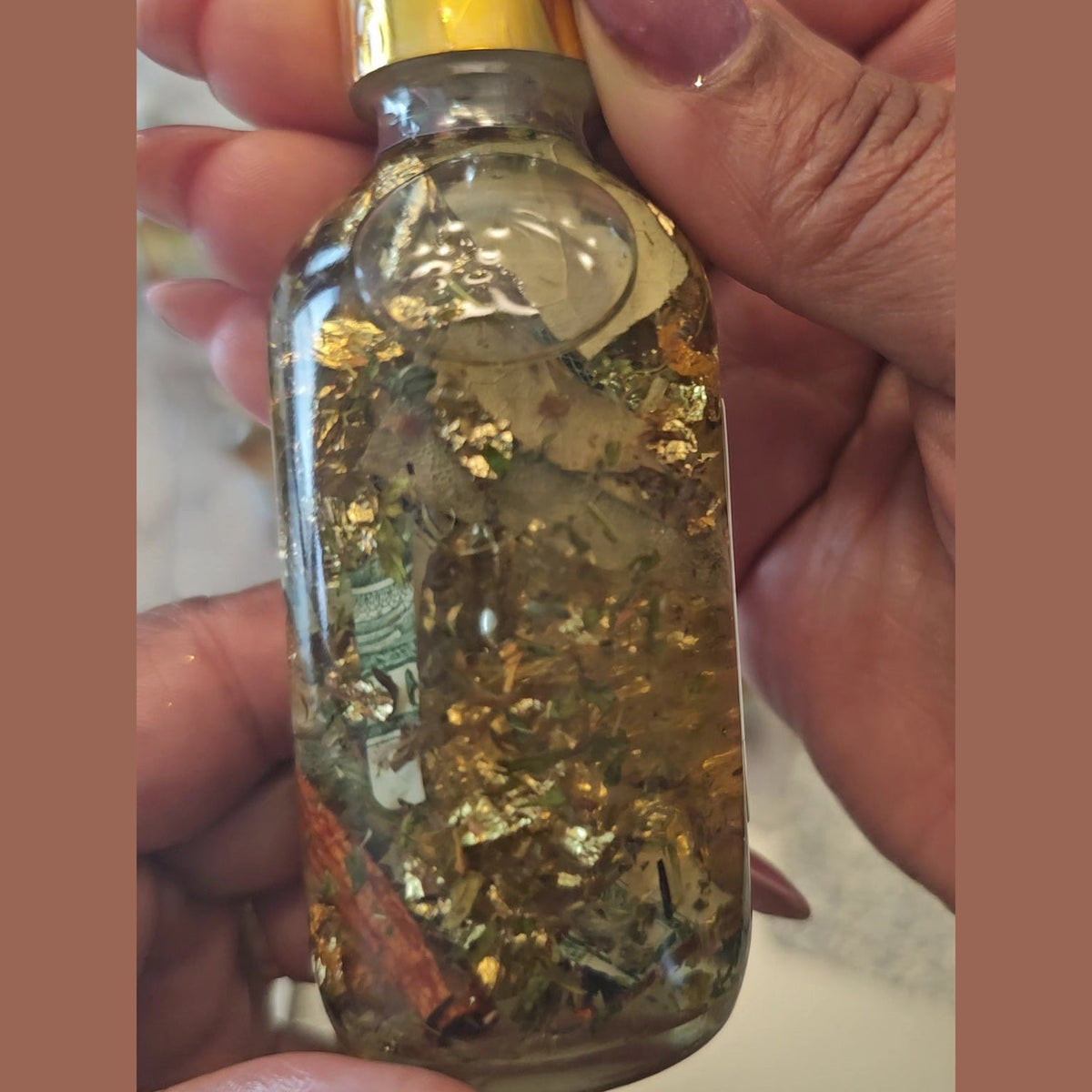 Glass bottle with gold leaf held by a hand. Fast Money Oil - Luxury Hoodoo Conjure Oil for Quick Cash & Prosperity