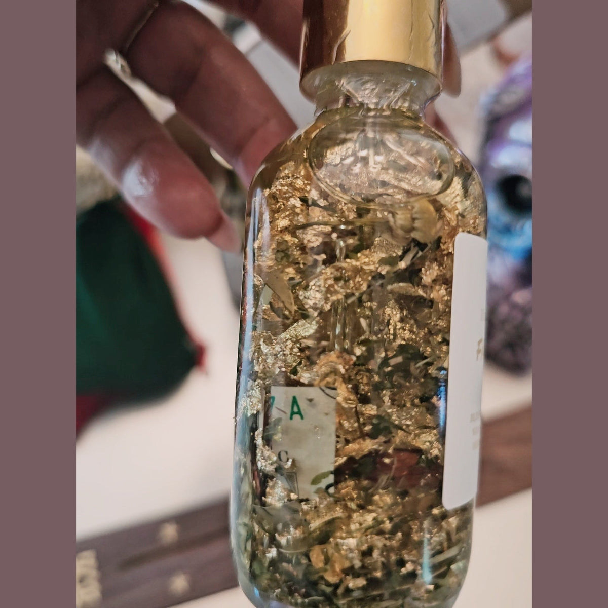 Glass bottle filled with gold flakes held by a hand Fast Money Oil - Luxury Hoodoo Conjure Oil for Quick Cash & Prosperity