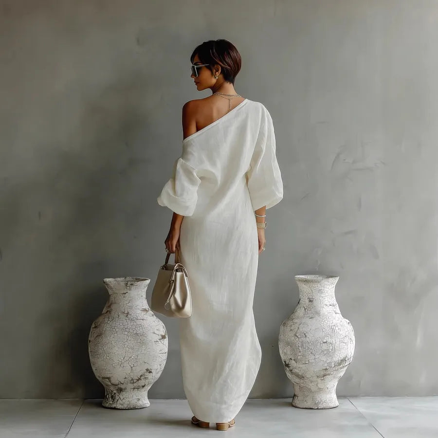 Woman in a white dress standing between two large vases against a gray wall.