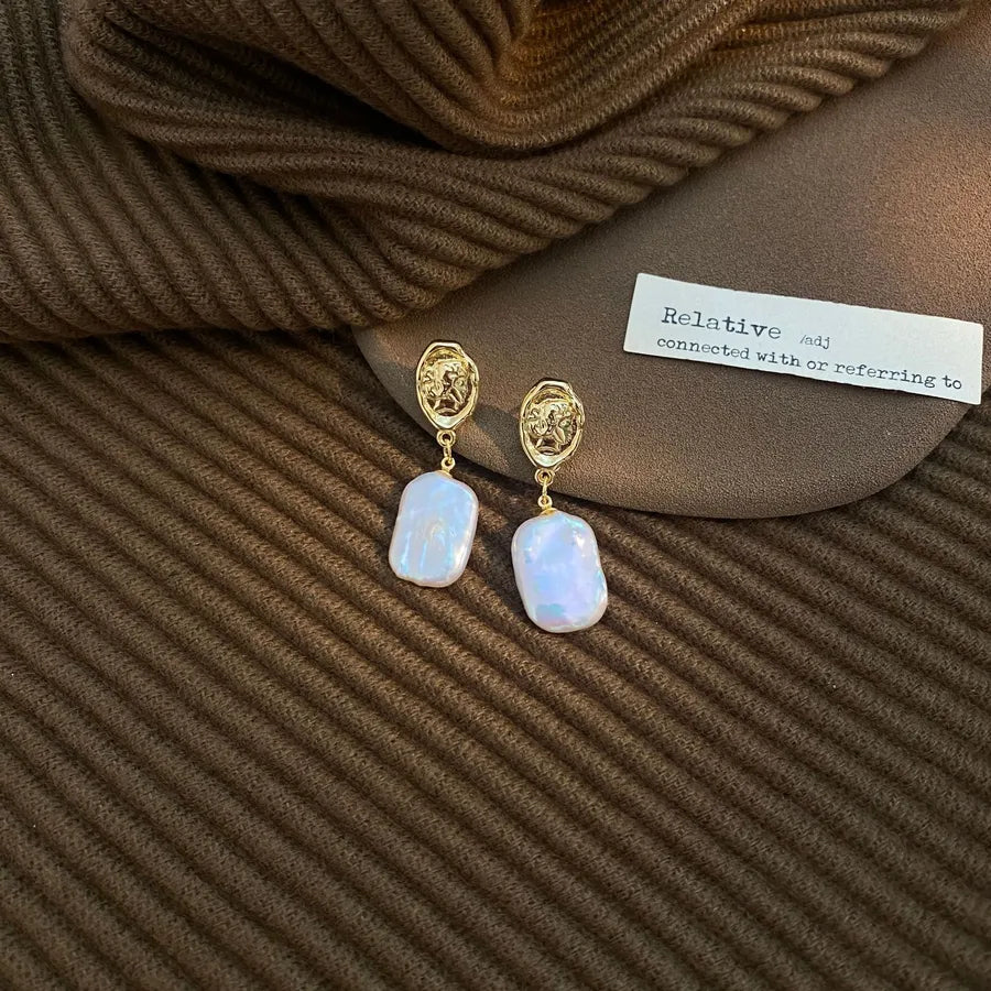 Gold earrings with white stones on a brown textured fabric background