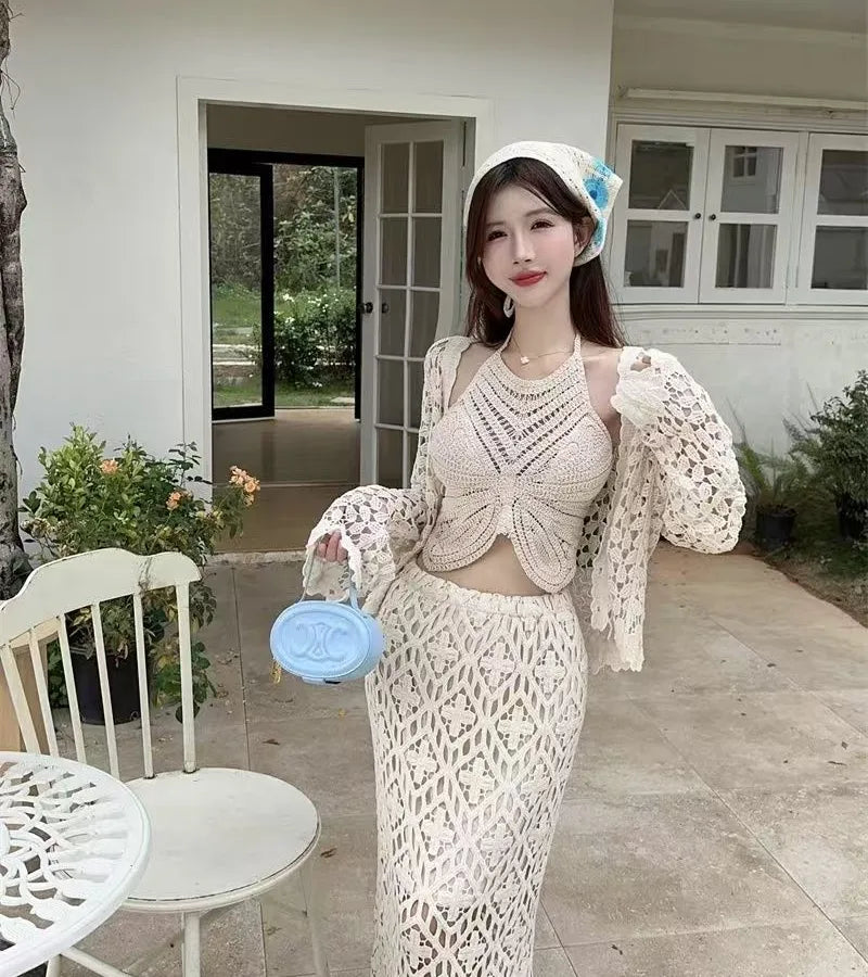 Woman in a white crochet outfit standing outdoors near a house.