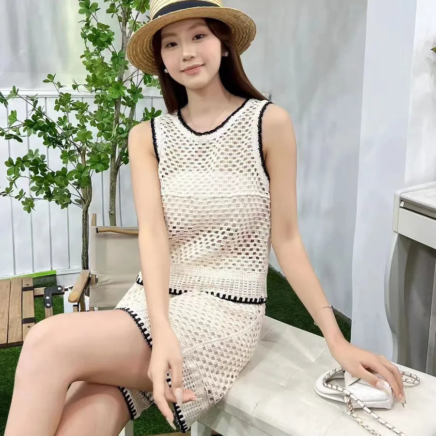 Woman wearing a white crochet dress and straw hat sitting outdoors.