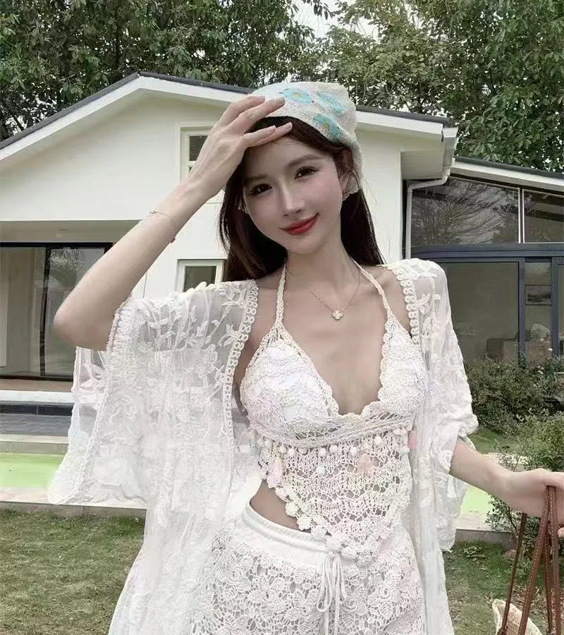 Woman in a white lace outfit posing outdoors with a building and greenery in the background