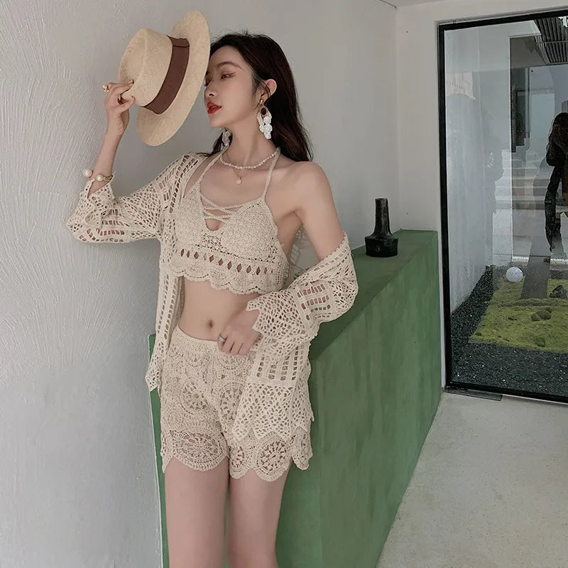 Woman in a beige crochet outfit holding a hat indoors.