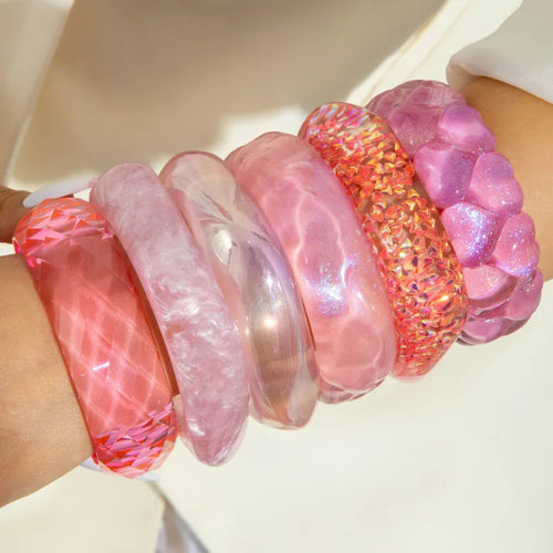 Close-up of a wrist wearing multiple pink and red bangles on a light background