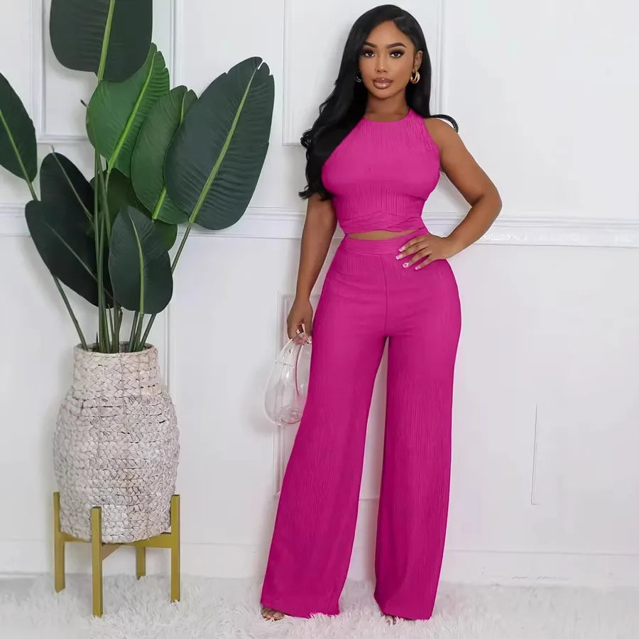 Woman in a pink outfit standing next to a potted plant against a white wall.