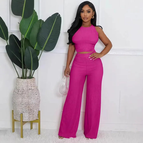 Woman in a pink outfit standing next to a potted plant against a white wall.