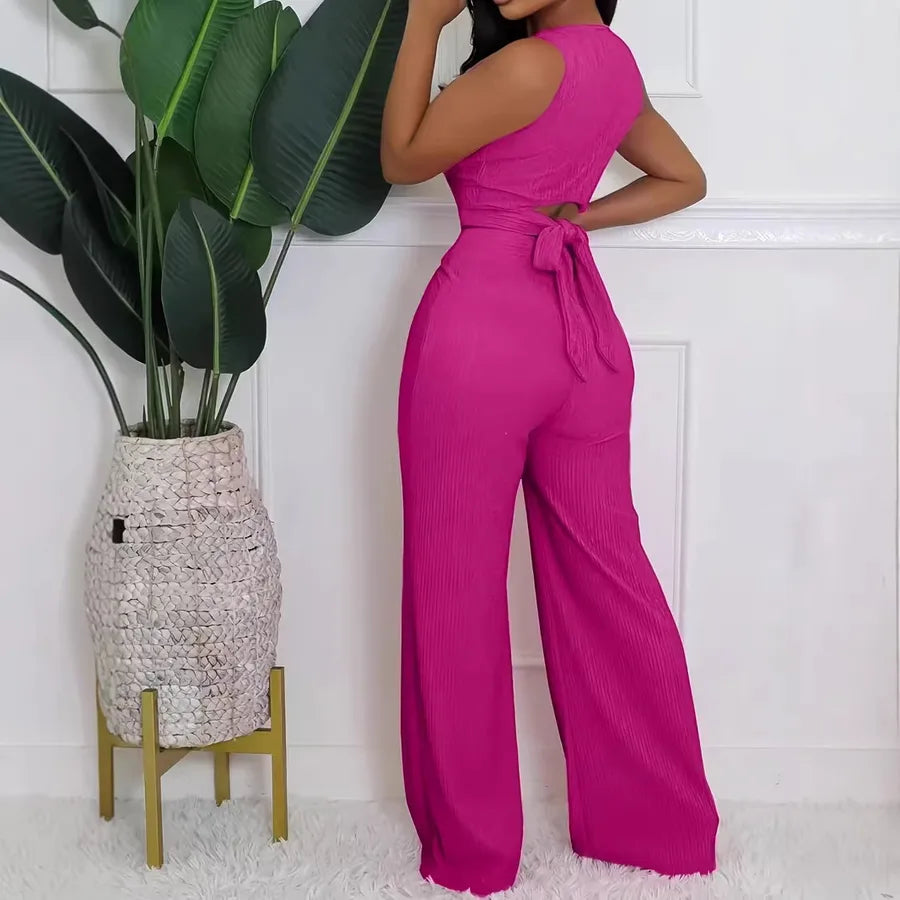 Woman wearing a bright pink jumpsuit standing next to a potted plant indoors.