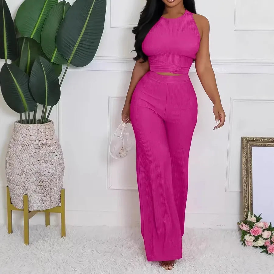 Woman wearing a bright pink outfit standing next to a plant and decorative items.