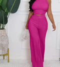 Person wearing a bright pink outfit standing in a room with a plant and white wall.