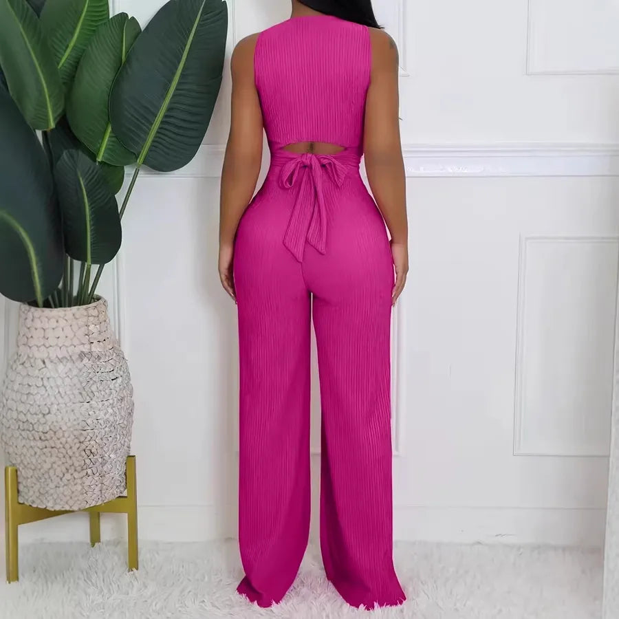 Person wearing a bright pink jumpsuit standing next to a plant indoors.