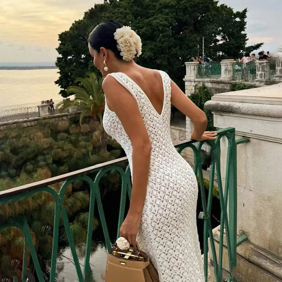 Woman in a cream color white dress standing on a balcony with a scenic view.