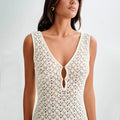 Woman wearing a cream colored white lace dress against a plain background