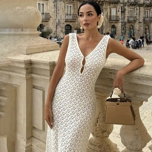 Woman in a cream white lace dress holding a beige handbag in an urban setting.
