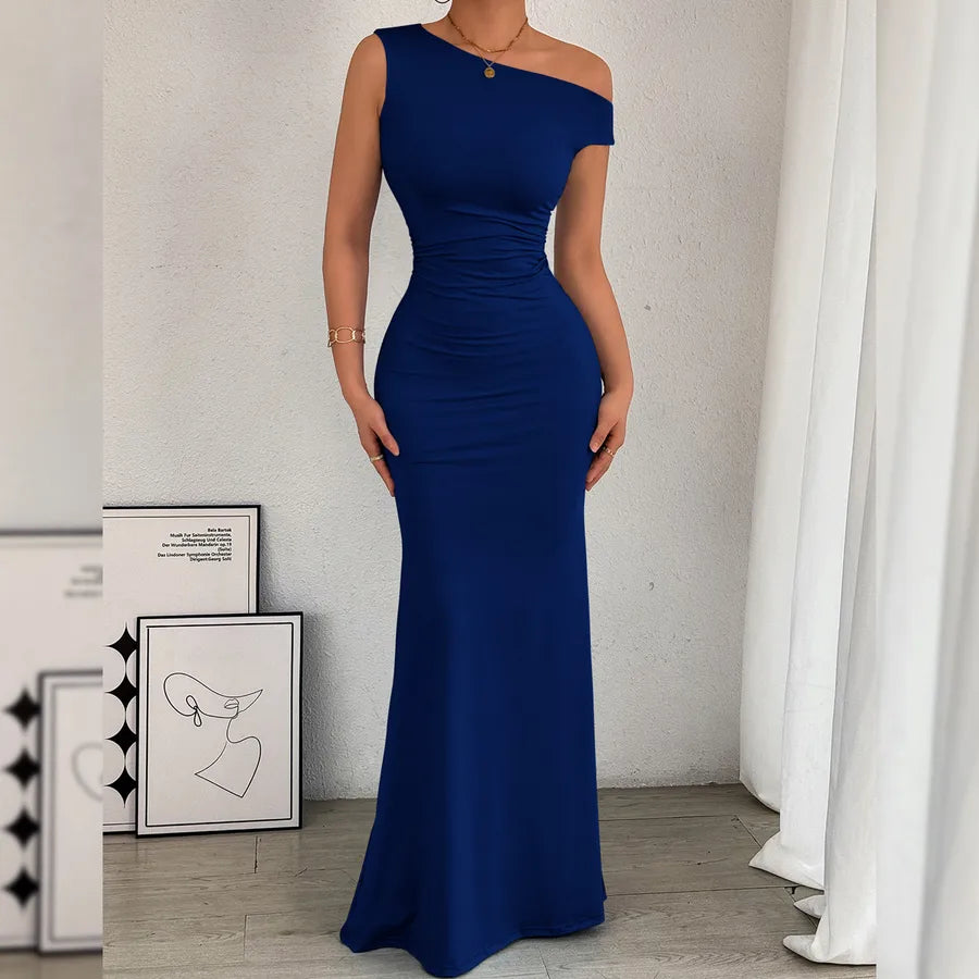 Woman wearing a blue off-shoulder gown in a room with white curtains and framed pictures.