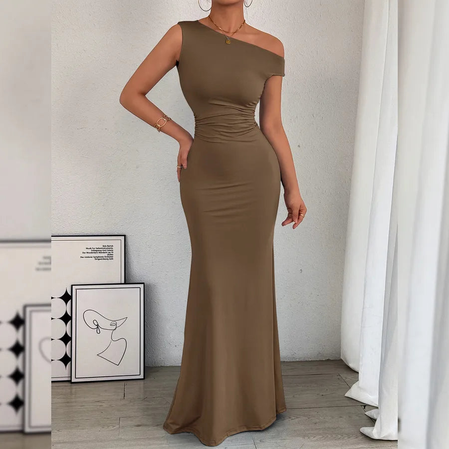 Woman wearing a brown one-shoulder dress in a minimalistic room.