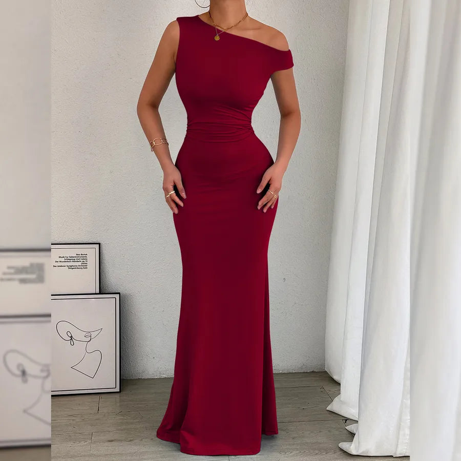 Woman wearing a burgundy off-shoulder gown in a room with white curtains.