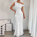 Woman wearing a white one-shoulder dress in a minimalistic room.