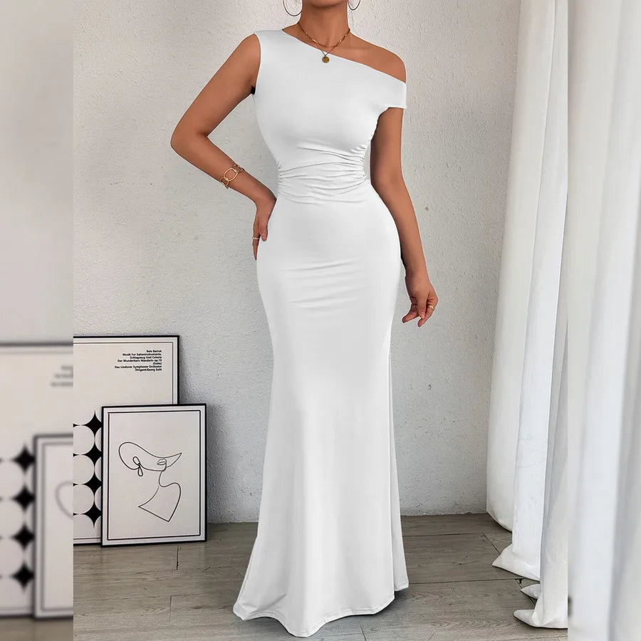 Woman wearing a white one-shoulder dress in a minimalistic room.