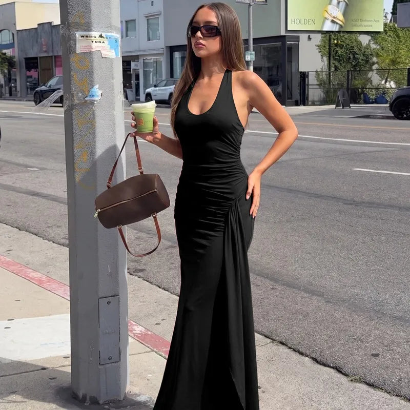 Woman in a black dress holding a brown handbag and a green cup on a city street.