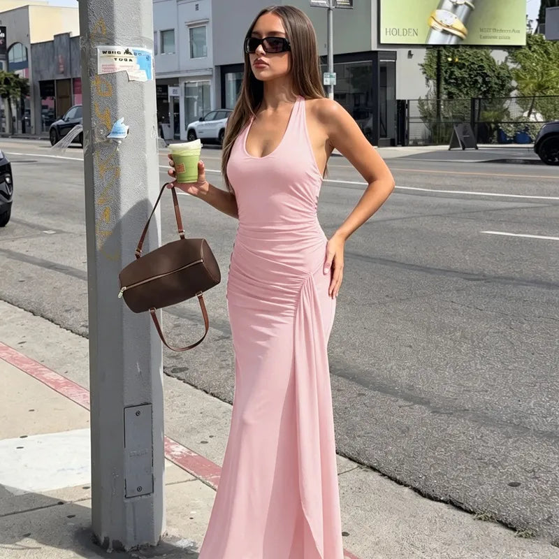 Woman in a pink dress standing on a city street holding a coffee cup.