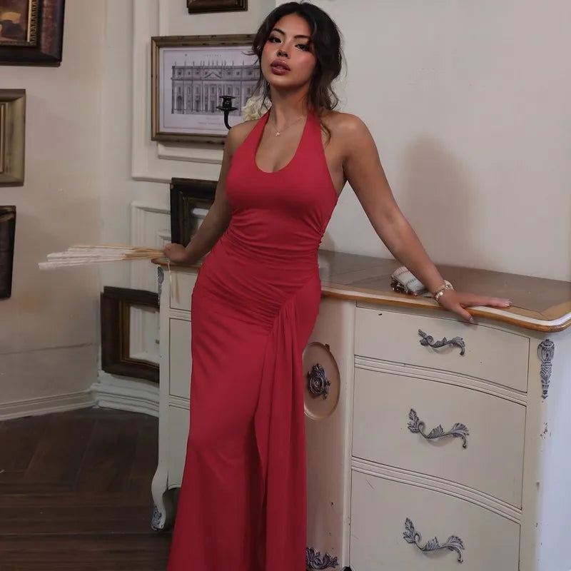 Woman in a red dress standing in a room with a dresser and framed pictures on the wall.