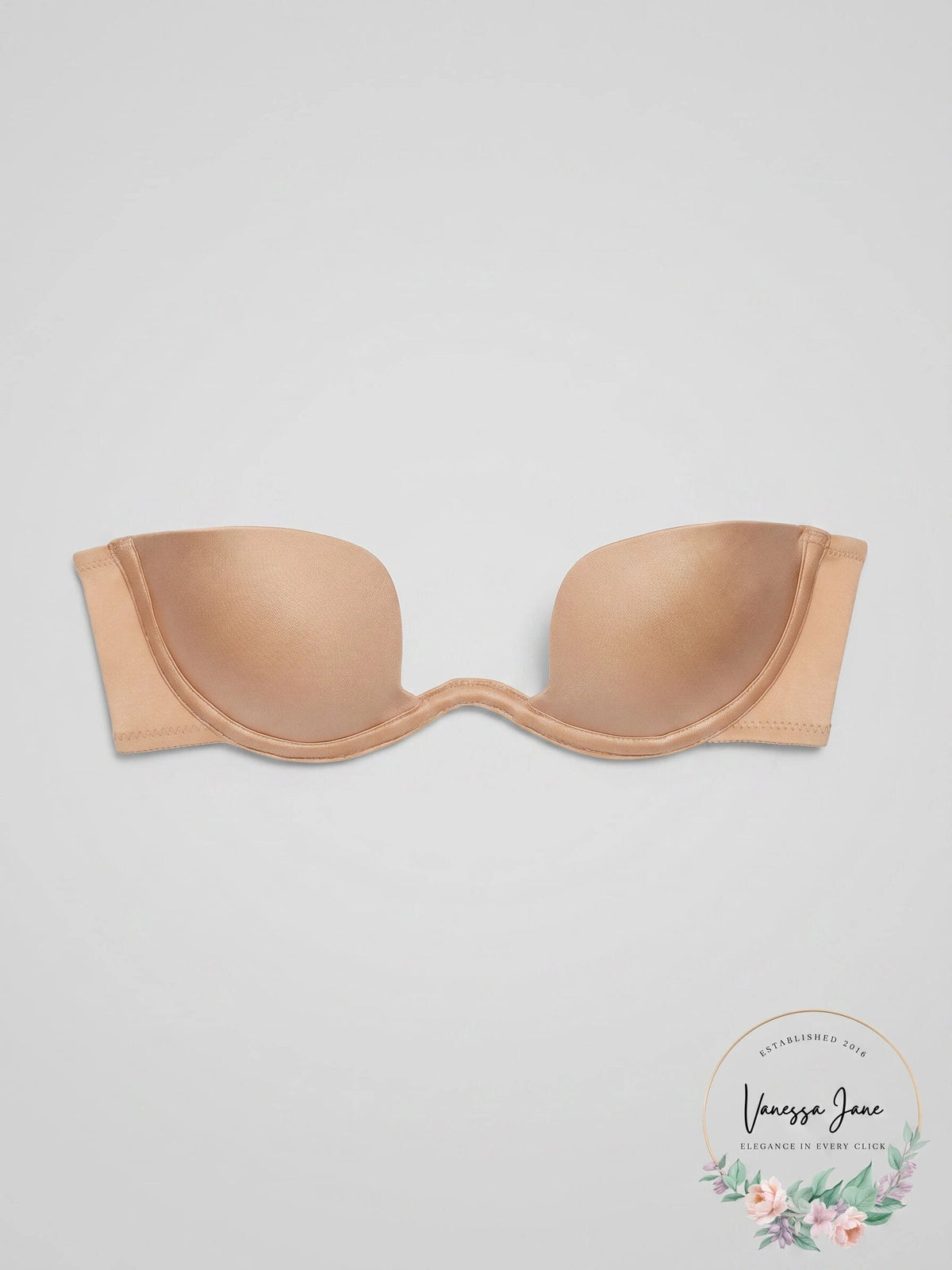 A strapless bandeau bra in a light peach-beige color, laid flat against a light gray background with a 'Vanessa Jean' brand watermark in the bottom right corner.
