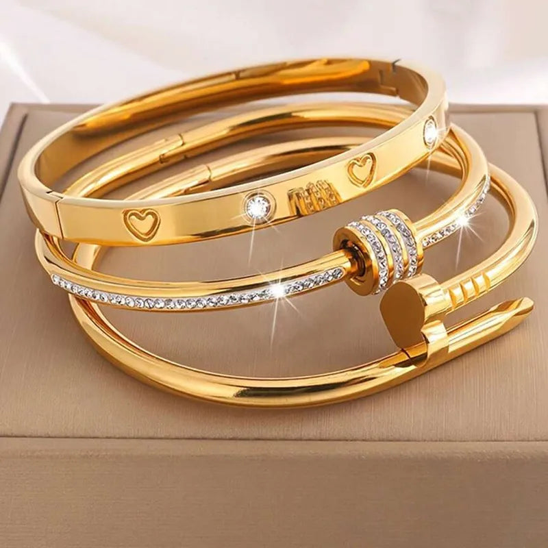 Gold bracelets with heart and diamond designs on a beige surface