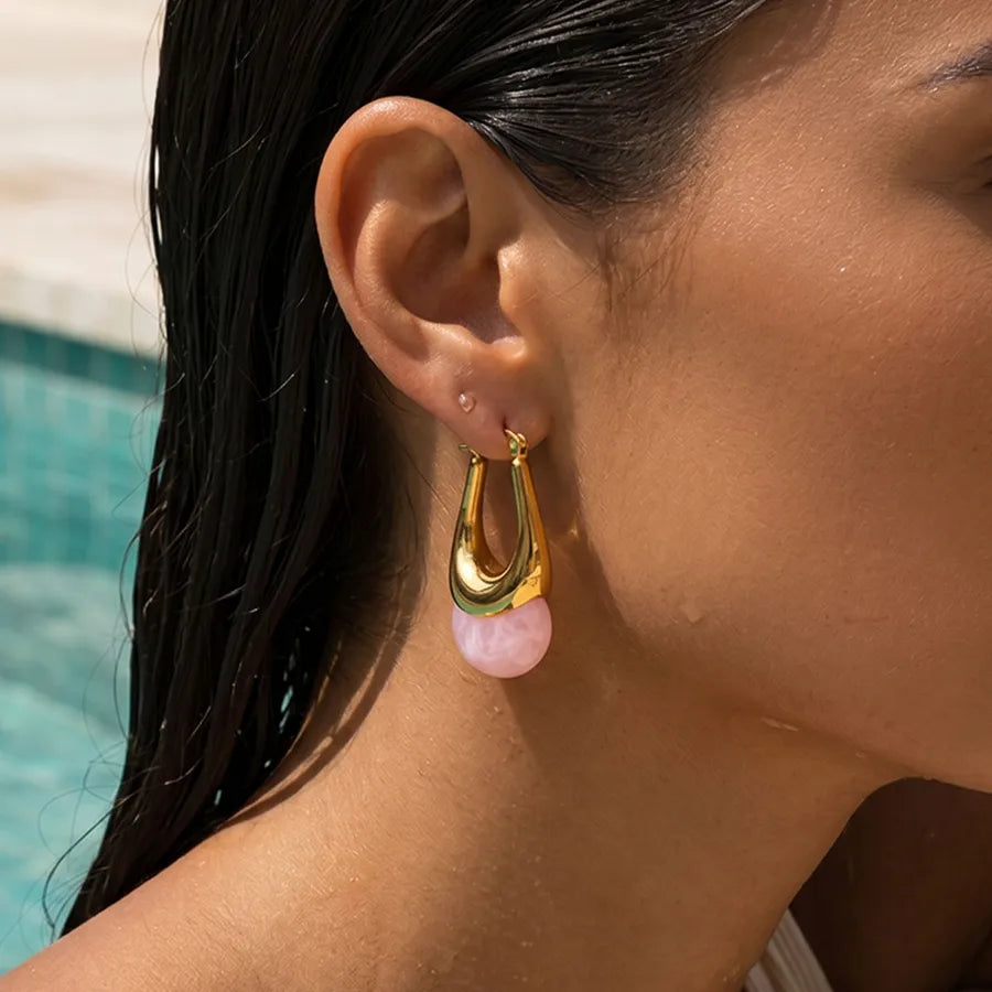 Close-up of a woman wearing gold hoop earrings with pink stones by a pool. Rose Quartz Stone Earrings