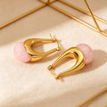 Gold hoop earrings with pink beads on a beige surface