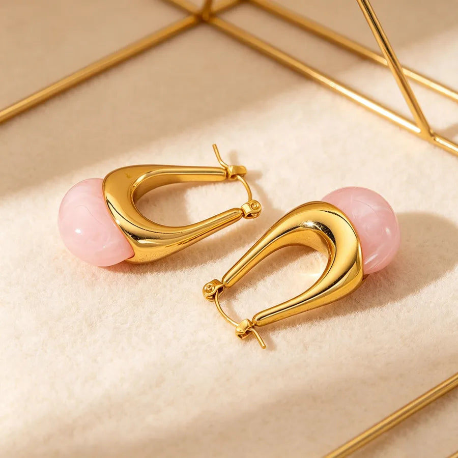 Gold hoop earrings with pink beads on a beige surface