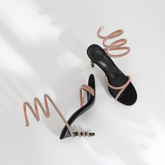 Black high-heeled shoes with rose gold straps on a white background