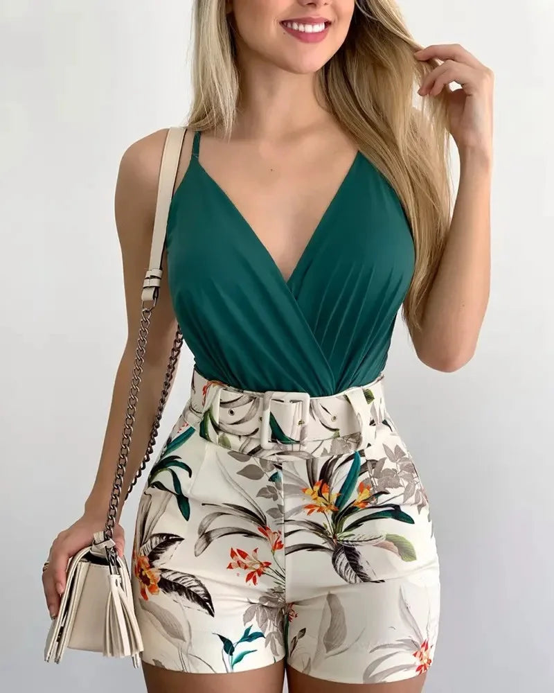 Woman wearing a green top and floral shorts with a gold clutch against a white background