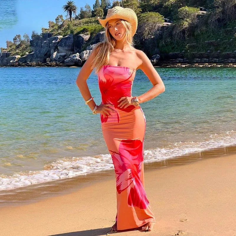 Woman in a colorful dress and hat standing on a beach with ocean and rocks in the background. Vacation resort dress