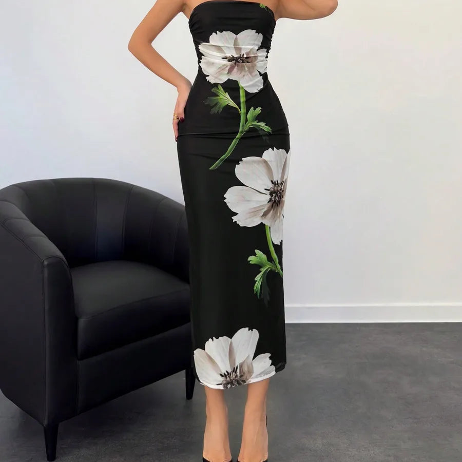 Black strapless dress with floral patterns worn by a person, sitting on a black chair against a white wall. Vacation resort dress