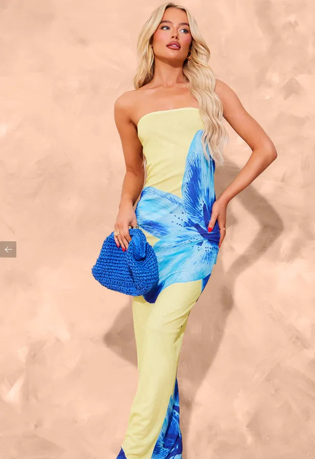Woman wearing a strapless dress with blue floral design against a beige background. Vacation resort dress