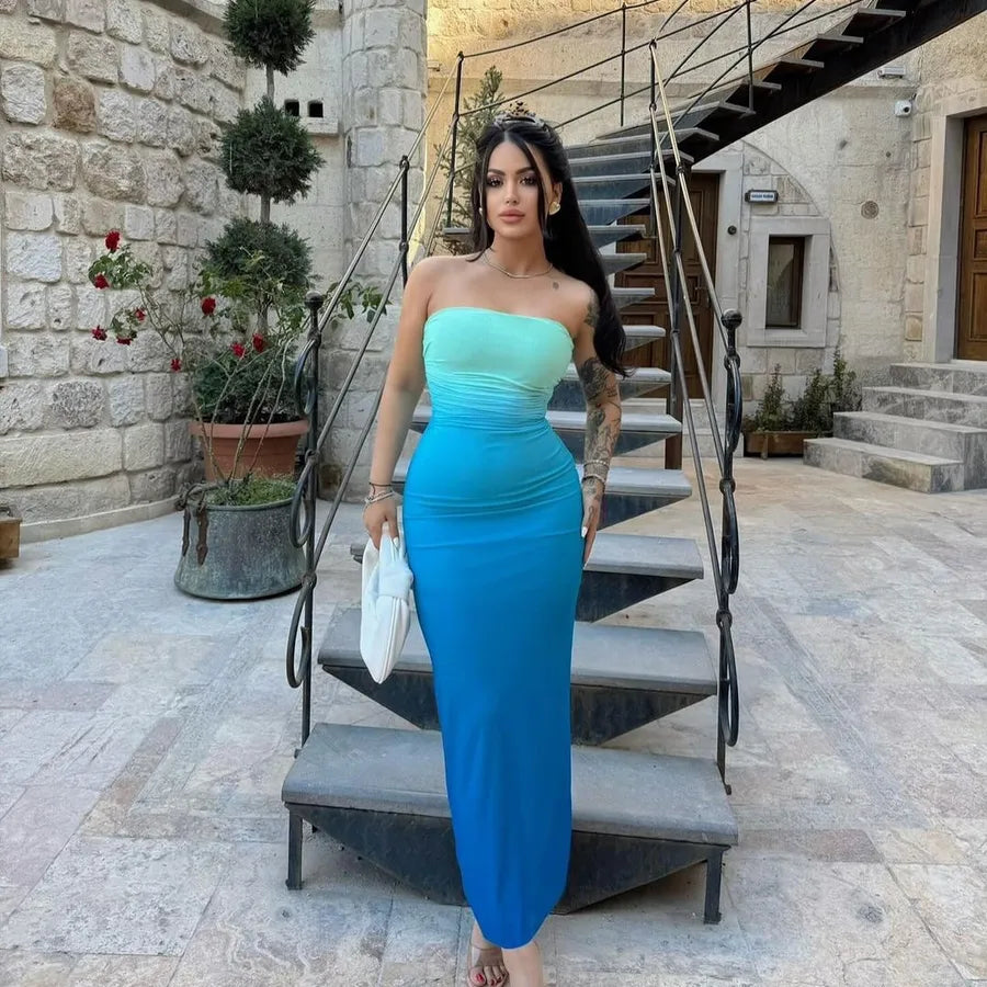 Woman in a strapless blue dress standing on stone steps with a stone building and plants in the background. Vacation resort dress
