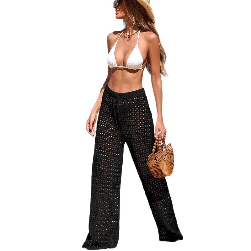 Woman wearing a white bikini top and black patterned pants, holding a straw bag on a white background Women's Hollow-Out Crochet Beach Cover-Up Pants – Sheer Wide Leg Swim Cover-Up Trousers for Resort & Vacation Wear beach cover up pants, crochet beach pants, hollow out pants, swim cover up pants, resort wear women, wide leg beach pants, crochet cover up, vacation outfit, poolside cover up, sheer beach pants, beachwear women, cruise outfit, tropical vacation clothes, boho beach pants, crochet trousers