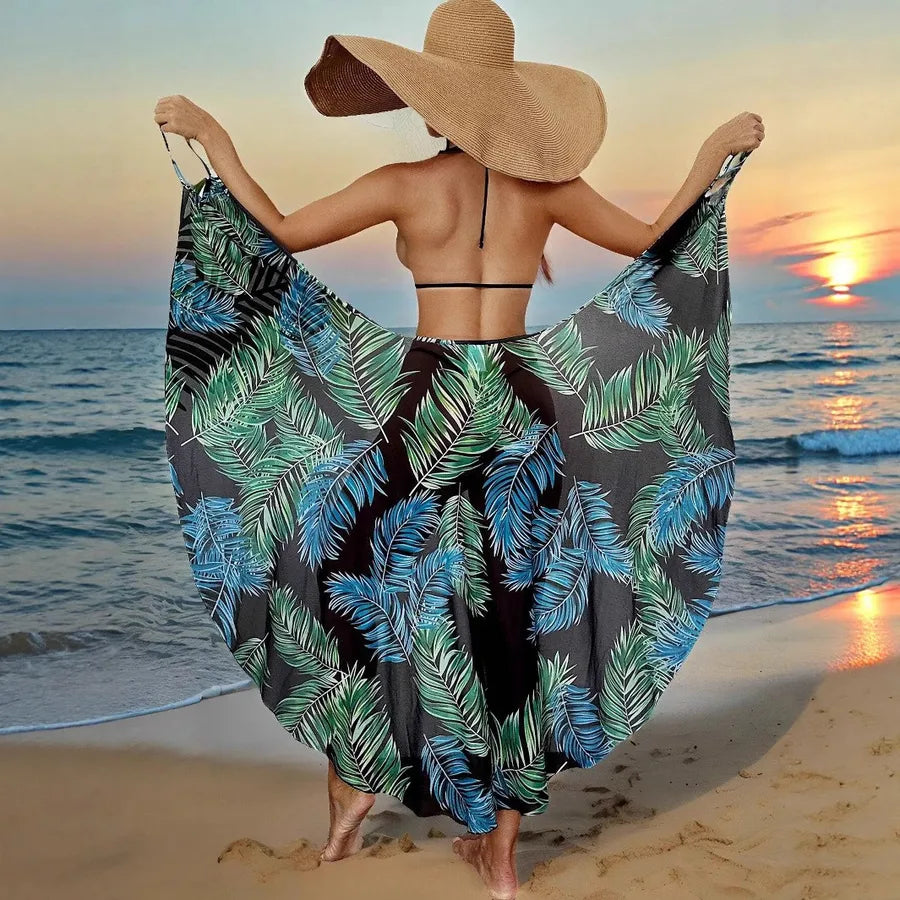 Woman on a beach at sunset wearing a large sun hat and a leaf-patterned sarong.