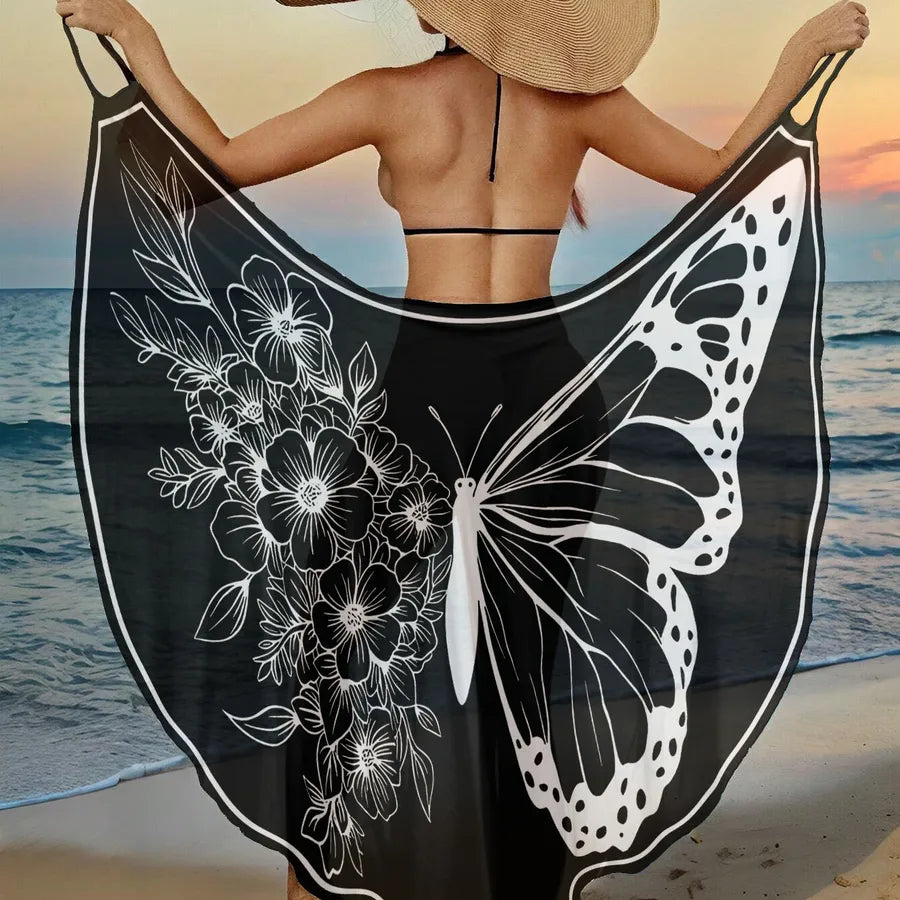 Woman holding a black and white butterfly-themed beach towel with ocean and sunset in the background