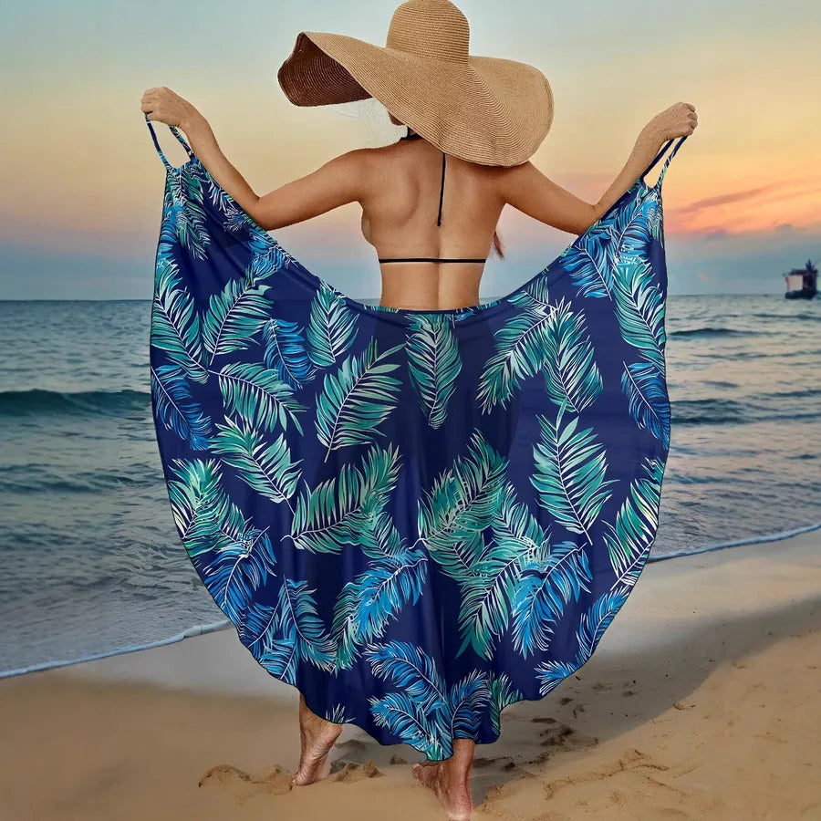 Woman on a beach wearing a blue leaf-patterned sarong and large straw hat.