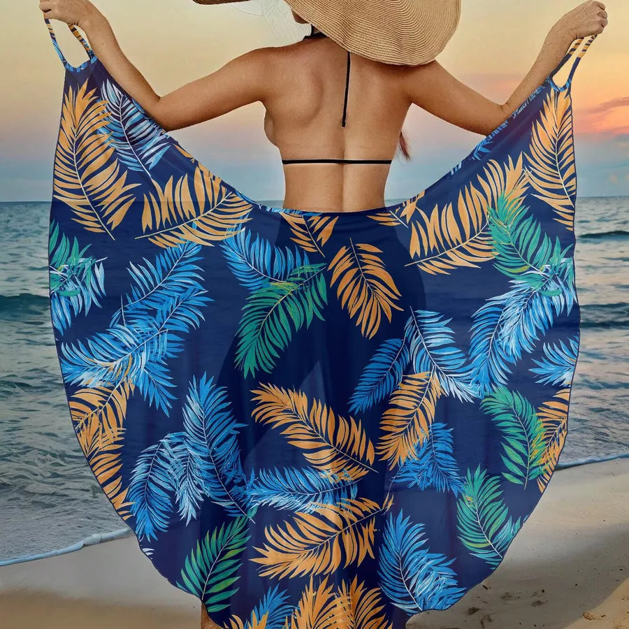 Person holding a blue tropical leaf patterned sarong on a beach at sunset.