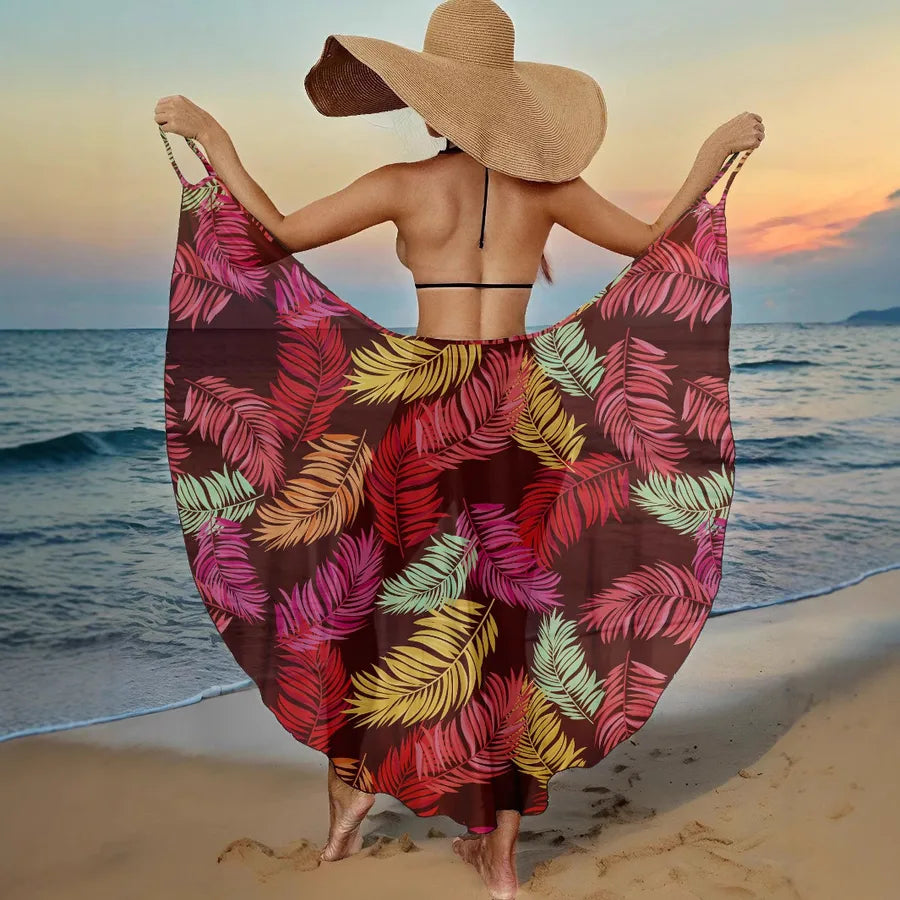 Woman on a beach with a colorful leaf-patterned sarong and straw hat.