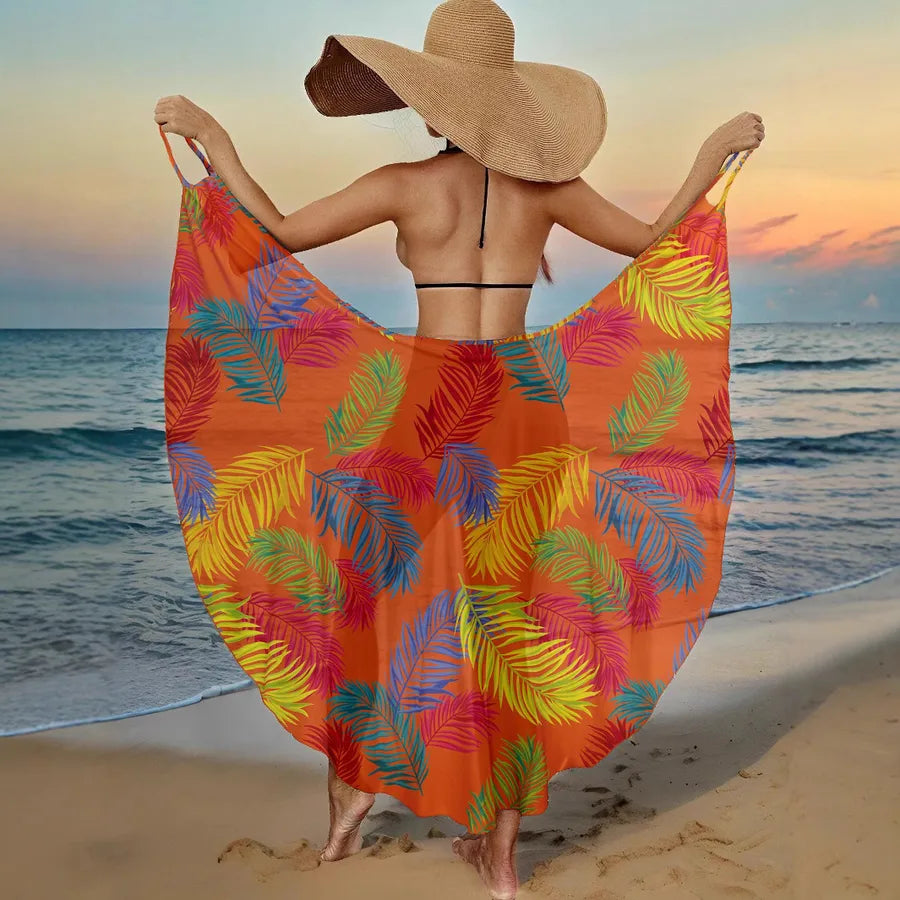 Woman on a beach wearing a colorful leaf-patterned sarong and a wide-brimmed hat.